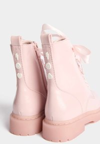 Botas de tobillo de imitación cuero rosa con un acabado brillante, frente con cordones, cierre de cremallera y acentos decorativos de rayo blanco y corazón.