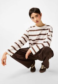 Valge pikkade varrukatega särk, millel on pruunid horisontaalsed triibud, kombineeritud pruunide triibuliste pükstega. Tumedad pruunid tennised heledate paeladega.