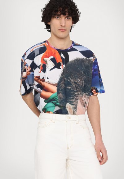 T-shirt grafico a maniche corte con un collage colorato di varie immagini su una base bianca, abbinato a pantaloni cargo chiari.