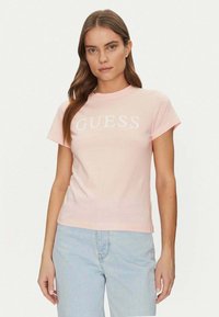 T-shirt di cotone rosa chiaro con colletto a giro e maniche corte, con il logo "GUESS" stampato in bianco sulla parte anteriore.