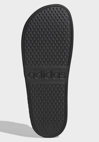 Black rubber sandal sole featuring a textured, diamond pattern with "adidas" embossed at the center. Durable and designed for grip.