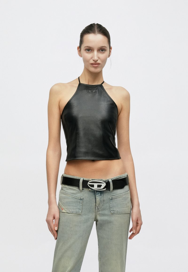 Μαύρο δερμάτινο τοπάκι με σχέδιο-χάλαρο, λεία υφή και μικρό ανάγλυφο λογότυπο στο ντεκολτέ, συνδυασμένο με ανοιχτό μπλε τζιν παντελόνι.