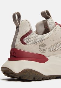 Sneaker impermeabile beige con pannelli in rete, dettagli rossi e suola in gomma testurizzata. Presenta un tassello per una facile vestibilità.