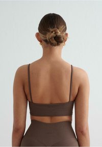 Bruine naadloze sportbeha met dunne straps, een aansluitend ontwerp en geribbelde textuur, van achteren weergegeven tegen een lichte achtergrond.
