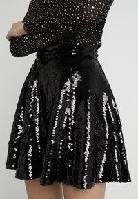 Falda negra con lentejuelas y silueta acampanada, que presenta lentejuelas brillantes y reflectantes, así como una cinturilla texturizada.