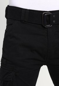 Svarta cargobyxor i ett hållbart tyg, synliga sömmar, ett brett bälte med en metallspänne och sidofickor på benen.