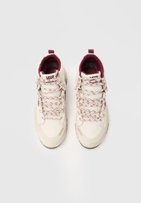 Beige värvi kõrge säärega Vans Gore-Tex tossud, millel on marooni värvi sisekate ja mustrilised paelad, asetatud valgele taustale kõrvuti.