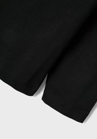 Črna bombažna majica s kratkimi rokavi, okroglo izrezom in urejenim šivom ob robovih. Gladka tekstura in minimalističen dizajn.