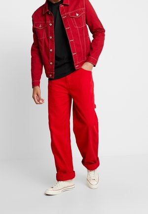 Punainen denim-takki hopeisilla yksityiskohdilla, yhdistettynä punaisiin cargo-housuihin ja krémivalkoisiin tennareihin. Musta T-paita alla, näkyvät käännetyt hihansuut.