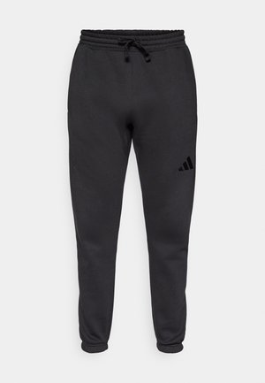Pantalons de survêtement noirs fuselés avec une taille élastique et un cordon de serrage, arborant un petit logo Adidas sur la cuisse supérieure droite.