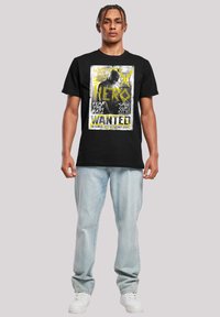 Svart bomull t-skjorte med et iøynefallende grafisk design i gult og hvitt. Kombinert med lys blå denimjeans og hvite joggesko.