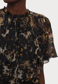 Blusa nera con un motivo floreale nei colori giallo, arancione e marrone. Collo arricciato, dettaglio con fiocco e chiusura con bottoni, maniche corte.