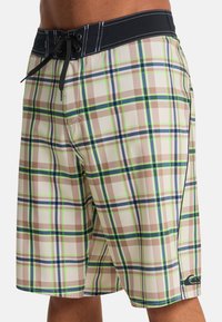 Καρό μαγιό σορτς σε μπεζ, πράσινο, μπλε και καφέ χρώμα, με μαύρη μέση, κορδόνι και πλαϊνή τσέπη. Ελαφρύ υλικό που στεγνώνει γρήγορα.
