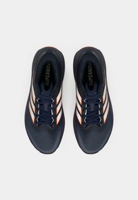 Granatowe buty do biegania z teksturowaną cholewką, z odblaskowymi srebrnymi paskami i pomarańczowymi akcentami, sznurowane, z amortyzowaną podeszwą.