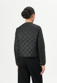 Black quilted jacket with a round neckline, long sleeves, and a cropped fit. Features diamond-shaped pattern and smooth texture.
