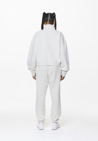 Felpa oversize grigio chiaro con colletto alto e pantaloni coordinati. Tessuto morbido e strutturato, vestibilità rilassata e polsini a costine sui polsi e alle caviglie.