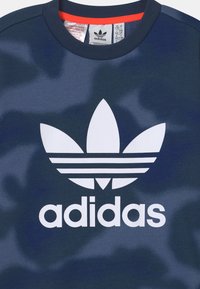 Marlové modré mikina s bílým logem Adidas a designem tří pruhů. Okruglý výstřih a jemná struktura. Uvnitř jsou viditelné štítky s pokyny k údržbě.