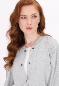 Grijze trui cardigan met ronde hals, drukknopen en een zachte textuur. Beschikt over een losse fit en geribbelde accenten langs de halslijn.