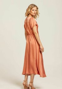 Persikofärgad satinklänning midi med korta ärmar, rynkad midja och utställd kjol. Den har en slät textur och en subtil lyster.