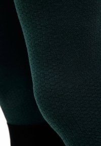 Nahaufnahme von strukturiertem dunkelgrünem Stoff auf einer gewölbten Oberfläche, mit gestricktem Muster und feinen Nahtdetails.