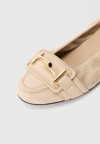 Beežist seemisnahast madala kontsaga jalanõu ümarate varvastega ja kuldse tooniga metallist pandlaga esimesel rihmal.