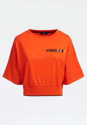 Korte mouwen oranje katoenen T-shirt met een zwarte #GUESS//81 print op de voorkant en een aansluitende tailleband. Gladde textuur, casual ontwerp.