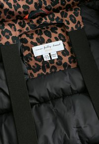 Brązowa tkanina z czarnym wzorem lamparta, wyposażona w czarną podszewkę wewnętrzną oraz metkę z instrukcjami pielęgnacji i informacjami o rozmiarze.