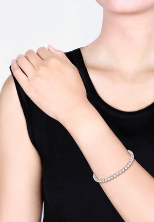 Sølvarmbånd med flere runde klare ædelsten, båret på en bar arm, med en glat, skinnende finish og delikat design.