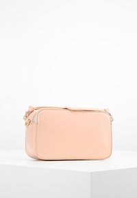 Persikofärgad lädercrossbodyväska med rektangulär form, dragkedjestängning och detaljer i guld; slät yta och minimalistisk design.