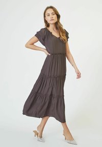 Rochie maxi de culoare maron închis, cu sleve scurte, plisate, eșarfe stratificate și decolteu în V. Material neted și fluid, cu buzunare laterale.