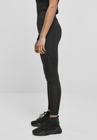 Leggings noirs avec une taille haute, dotés de panneaux en maille texturée sur les côtés et d'une silhouette ajustée. Associés à des bottines noires.