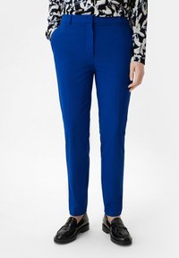Niebieskie dopasowane spodnie o gładkiej fakturze, o wąskim kroju i bocznymi kieszeniami. Połączone z czarnymi loafersami i wzorzystą bluzką.