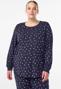 Marinblå pyjamaströja med lång ärm och mönster av rosa och vita hjärtan. Har rund halsringning och en avslappnad passform, tillverkad av mjukt bomullstyg.