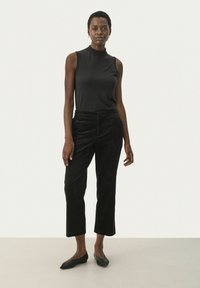 Black sleeveless top with a high neckline paired with black corduroy pants. The pants feature a straight cut and elastic waistband.