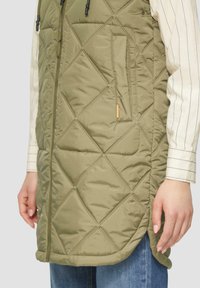 Gestepptes olivgrünes Weste mit hohem Kragen, Seitentaschen und Kordelzug. Das Material hat eine glatte, glänzende Textur und weist Rautenmuster auf.