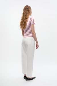 Gestreiftes rot-weißes enges T-Shirt, kombiniert mit lockeren weißen Hosen, von hinten betrachtet. Schwarze spitze Ballerinas komplettieren das Outfit.