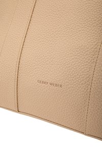 Superficie in pelle beige con texture e finissime cuciture, con "Gerry Weber" impressa al centro del pannello.