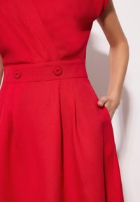 Czerwona lniana sukienka z dekoltem kopertowym, krótkimi rękawami, dwoma guzikami z przodu, plisami w talii i bocznymi kieszeniami.