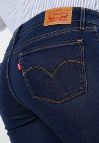 Tmavě modré džíny z denimové látky s hnědou koženou nášivkou „Levi Strauss & Co.“ na zadní straně, žlutým prošíváním a charakteristickým designem zadní kapsy.