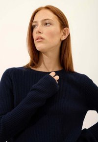 Granatowy sweter żebrowany z pełnymi rękawami i otworami na kciuki, z okrągłym dekoltem i miękką teksturą, na jednolitym białym tle.