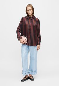 Cămașă cu nasturi în dungi negre și burgundy, cu guler, asortată cu pantaloni bleu deschis, decorați cu aplicații florale și pantofi slip-on negri.