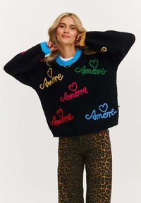 Czarny oversize sweter z wielokolorowym haftem "Amore", z prążkowanymi mankietami w niebieskim i pomarańczowym kolorze, zestawiony z spodniami w panterkę.