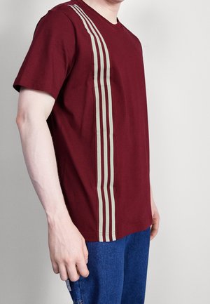 T-shirt bordeaux à manches courtes, présentant des rayures verticales beiges le long du côté gauche, fabriqué en tissu de coton doux, avec un col rond classique.