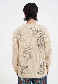 Beige geripptes Sweatshirt mit großen Grafikdrucken in Schwarz und Grau, in lässiger Passform und mit Rundhalsausschnitt.
