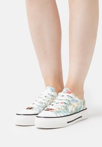 Sneakers met bloemenpatroon en een witte canvas bovenkant, voorzien van een platformzool en zwarte strepen, veterd met witte veters.