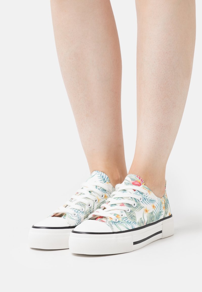 Sneakers met bloemenpatroon en een witte canvas bovenkant, voorzien van een platformzool en zwarte strepen, veterd met witte veters.