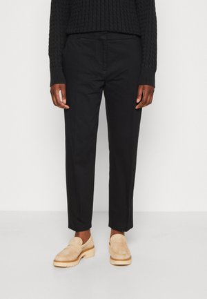 Pantalons noirs sur mesure avec une texture lisse, un design à jambes droites et une taille mi-haute. Associés à des chaussures à enfiler en daim beige.