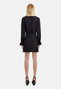 Svart klänning med långa ärmar, samlad midja och utsvängd kjol. Slätt tyg, minimalistisk design, ankelhöga blockklackskor.