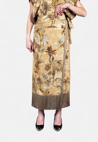 Gonna di satin oro con stampa di palme, caratterizzata da frange all'orlo. Indossata con tacchi alti neri, che mettono in risalto un design elegante e aderente.