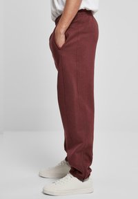 Pantaloni de trening burgund cu un elastic în talie, buzunare laterale și tivuri înguste. Purtați cu adidași albi, evidențiind o croială relaxată și confort.